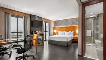 A hotel room with a large bed, a desk with a chair, a TV, and a shower area.