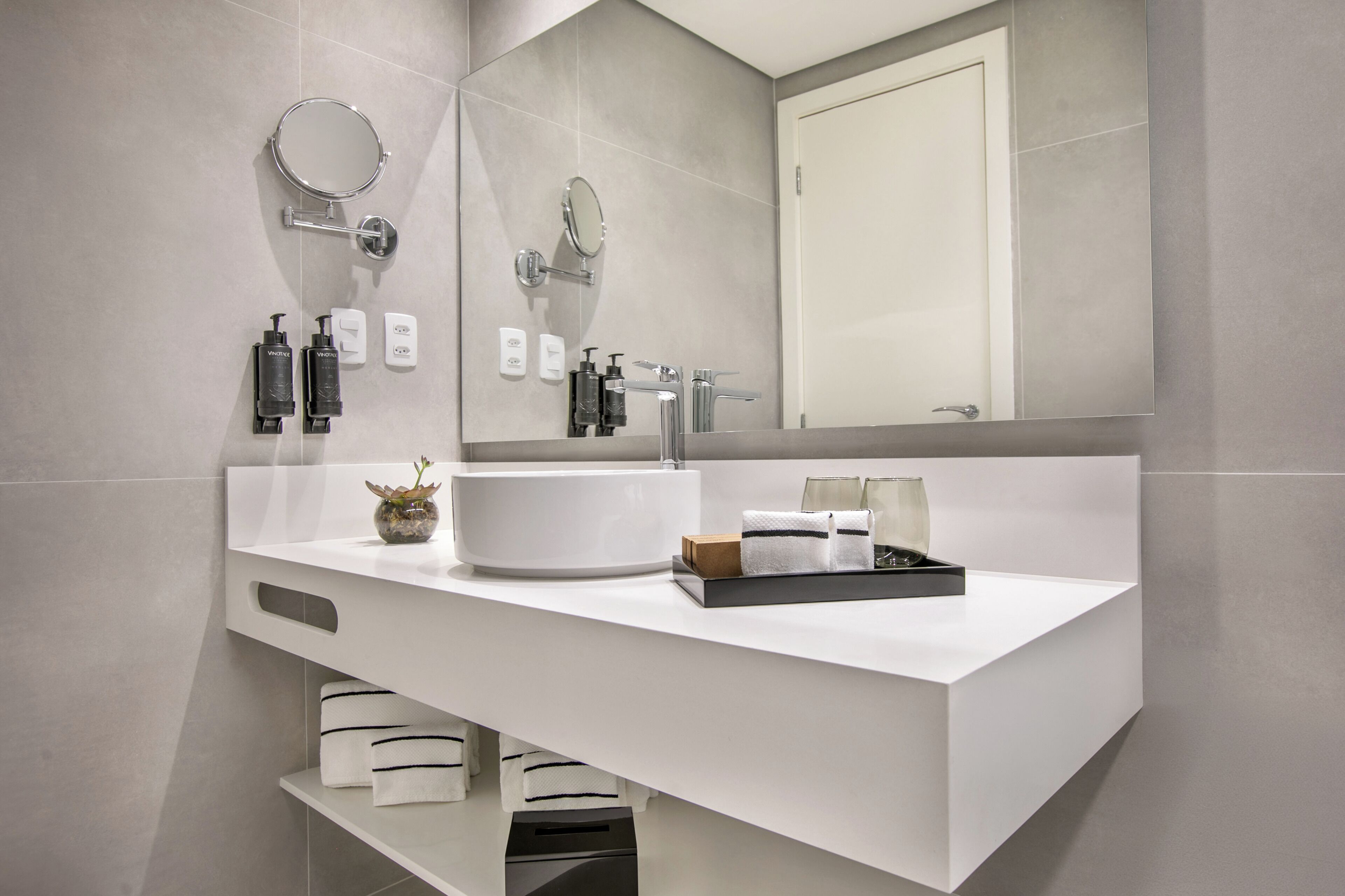 A modern bathroom with a white vanity, two sinks, a large mirror, and a towel rack.