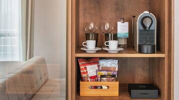 Una estantería de madera con plantas en macetas, tazas de café, una cafetera y un refrigerador lleno de bebidas.