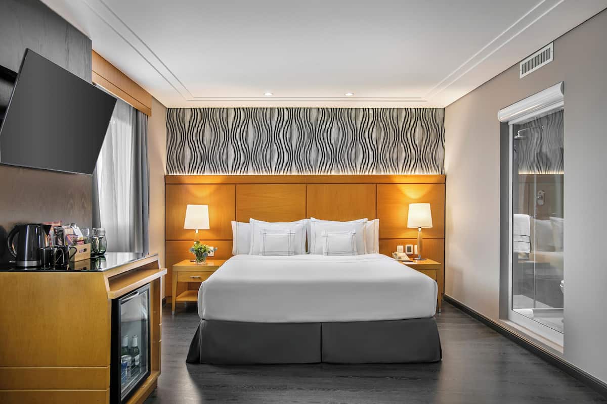 Ein Hotelzimmer mit Bett, Nachttischen, Fernseher, Minibar und einem großen Fenster.