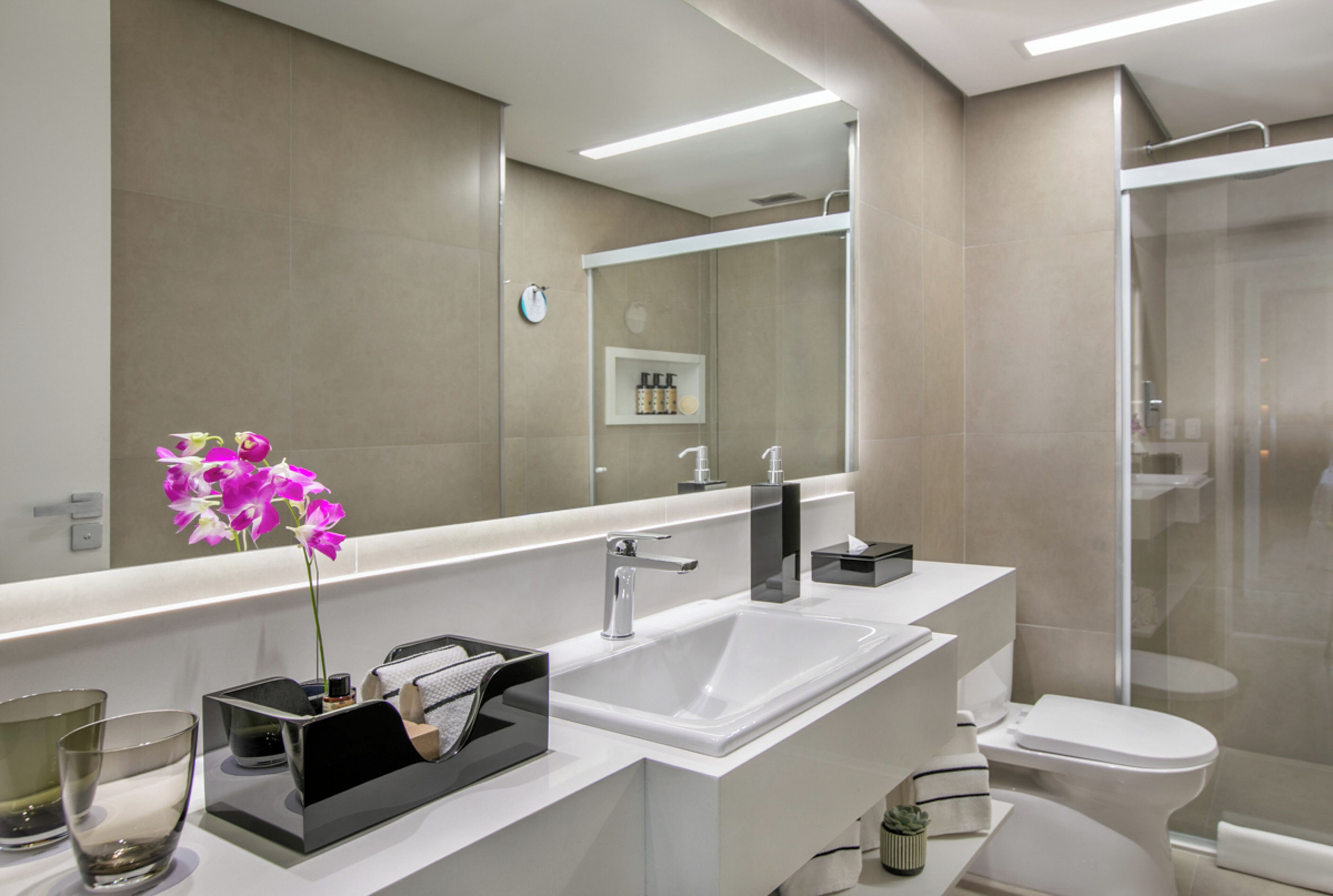 Un baño moderno con un espejo grande, un lavamanos, un inodoro y una zona de ducha.