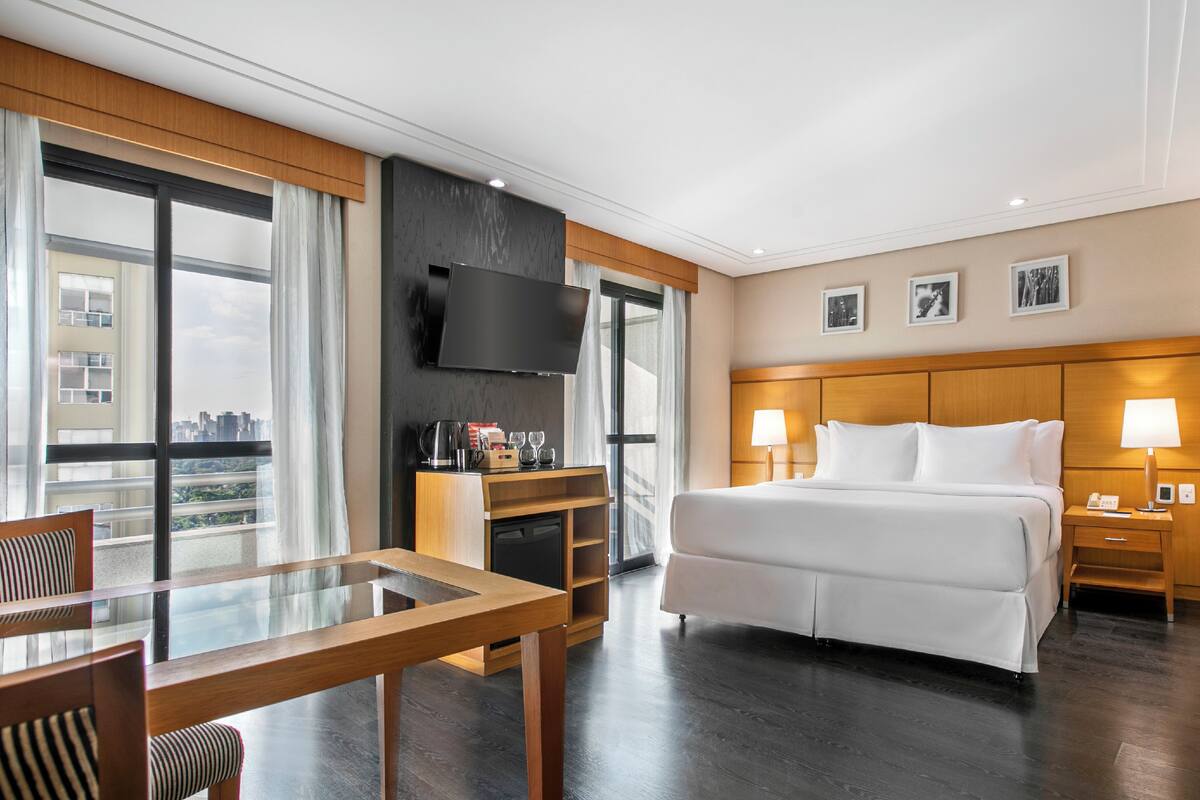 Ein Hotelzimmer mit Bett, Fernseher, Schreibtisch mit Stuhl, Nachttisch und Blick auf die Stadt.