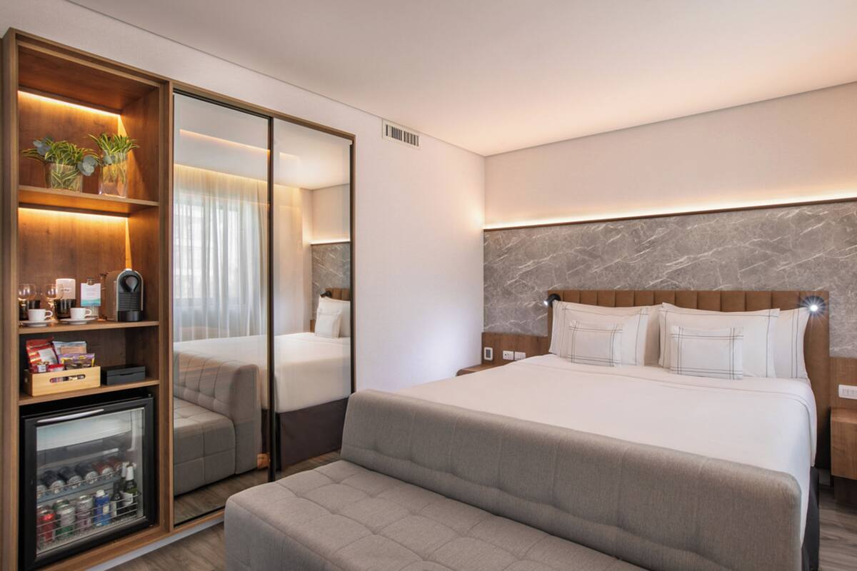 Ein modernes Hotelzimmer mit einem großen Bett, einer Sitzecke, einer Minibar und einem Spiegel.