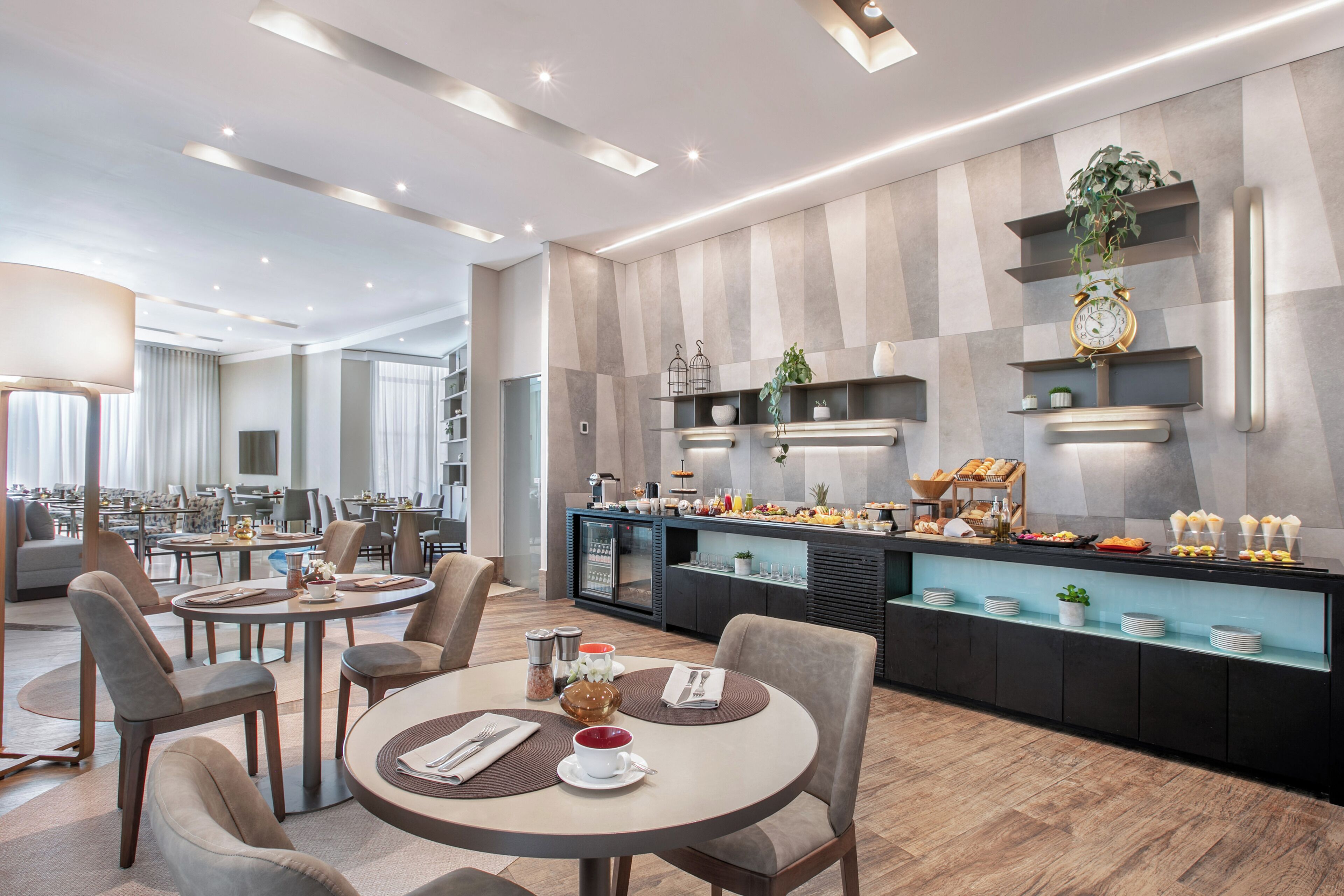 A modern hotel dining area with round tables, chairs, and a buffet counter.