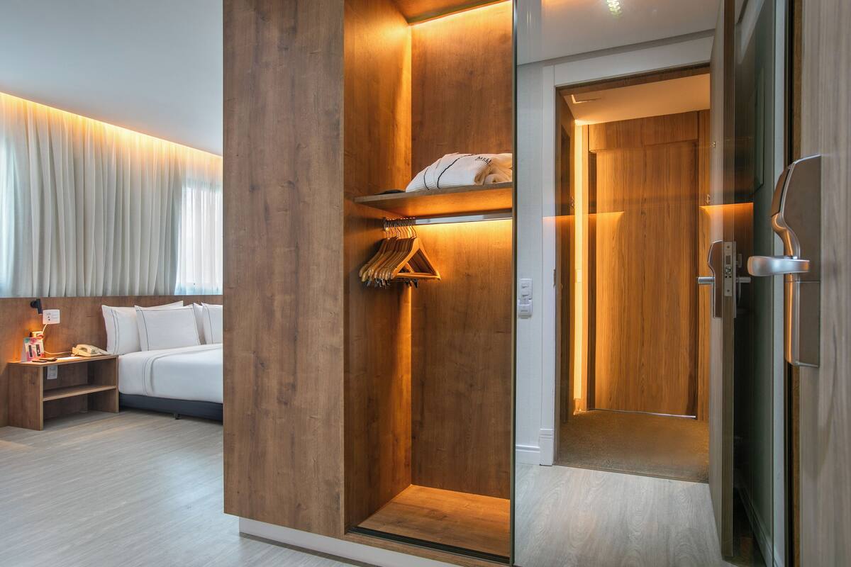 Ein modernes Hotelzimmer mit einem Holzschrank, einem Bett mit weißer Bettwäsche und einem Nachttisch mit Lampe und Telefon.