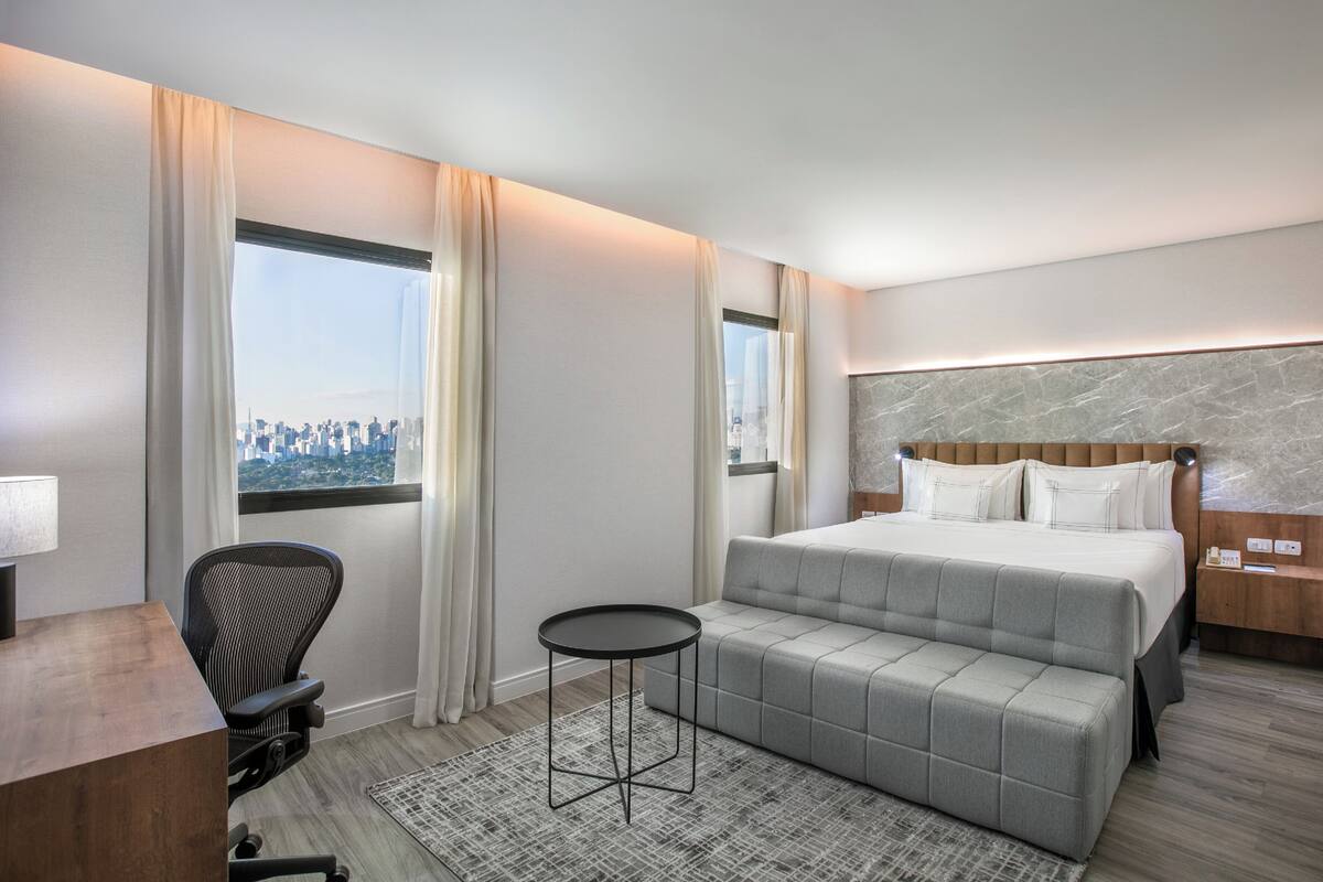 Ein Hotelzimmer mit einem Bett, einem kleinen Tisch, einem Stuhl und Blick auf die Stadt.