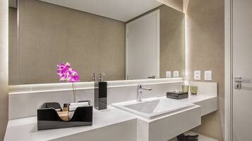 A modern bathroom with a large mirror, white sink, and a black soap dispenser.