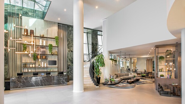 A spacious lobby with a marble reception desk, a staircase with a glass railing, and a seating area with sofas and a coffee table.