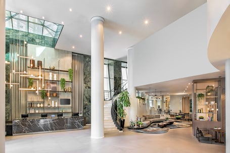 A spacious lobby with a marble reception desk, a staircase with a glass railing, and a seating area with sofas and a coffee table.