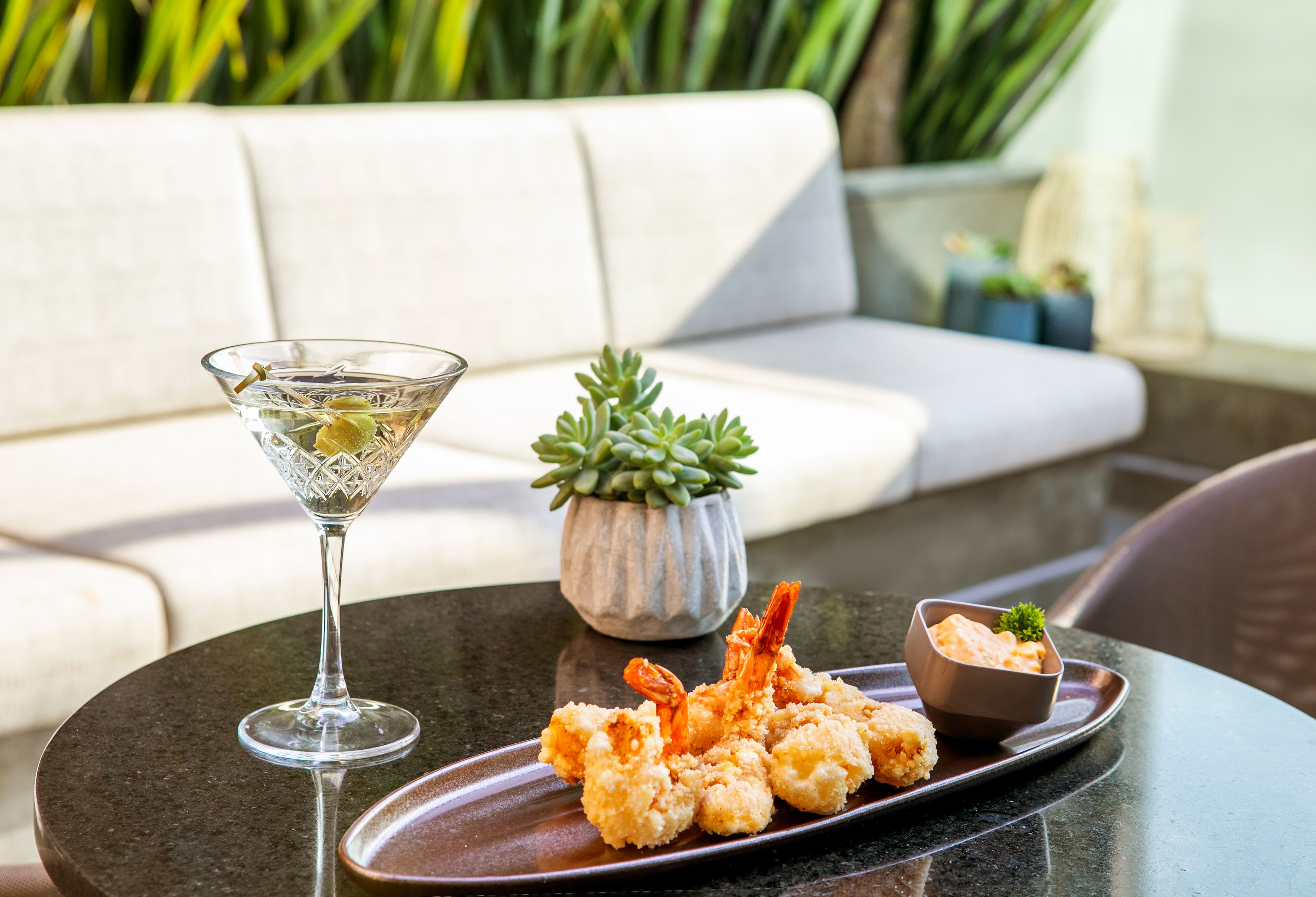 A dining table with a plate of fried shrimp, a martini glass, and a small potted plant.