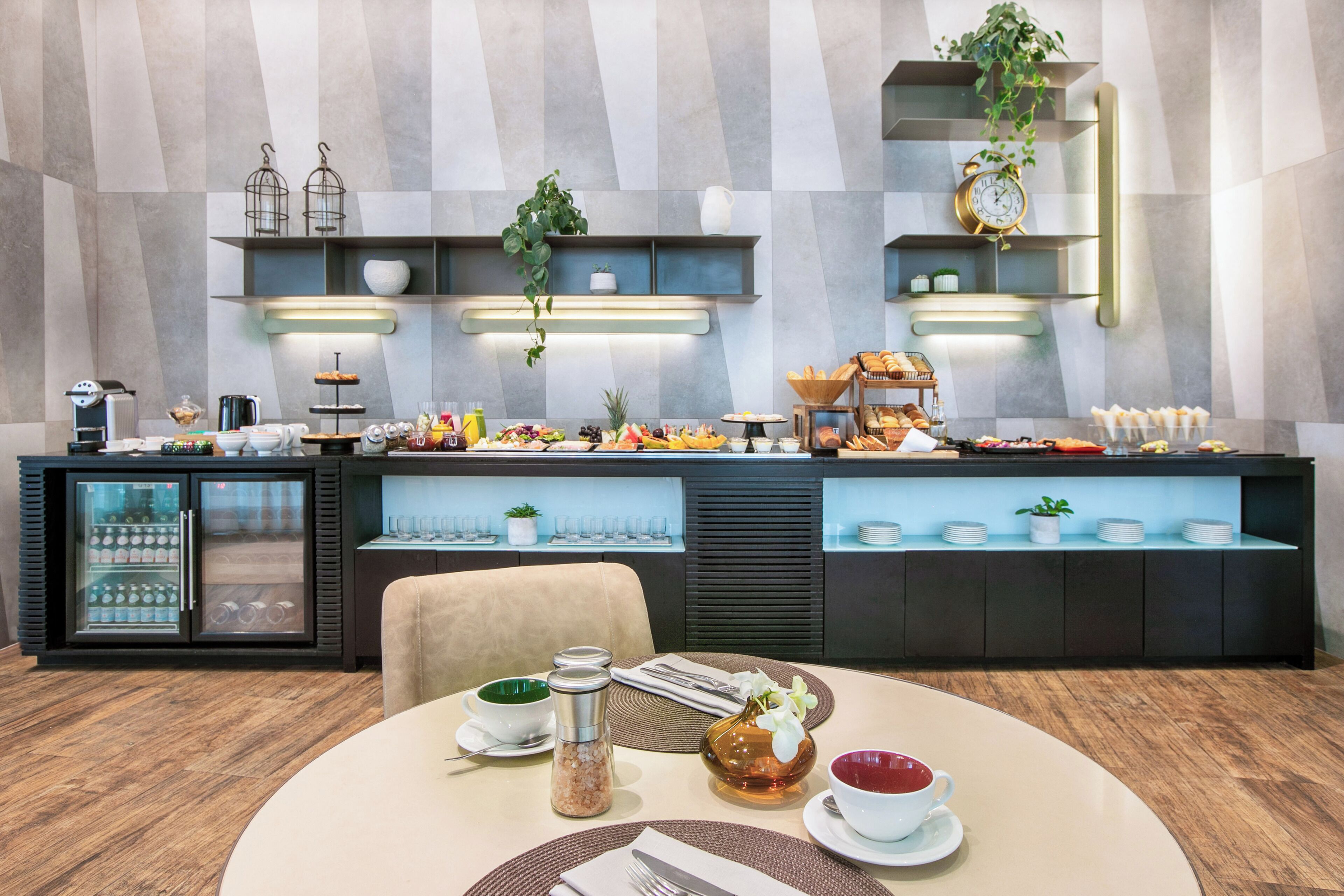 Un bufé de desayuno con diversas opciones de comida, una máquina de café y un refrigerador.