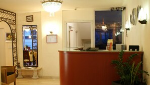 A reception area with a wooden reception desk, a potted plant, a mirror, and a chandelier. - Bahn Hotel (Düsseldorf)