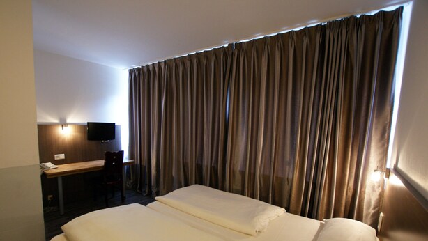 A hotel room with a bed, a desk, a chair, and a television. - Bahn Hotel (Düsseldorf)