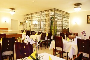 Zona pranzo con sedie e tavoli di legno, un divisorio decorativo e un lampadario.