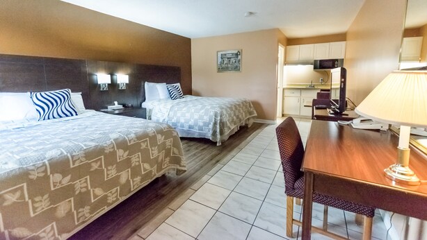 Habitación de hotel con dos camas, una mesa de comedor, una silla y una zona de cocina.