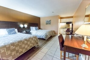 A hotel room with two beds, a dining table, a chair, and a kitchen area.