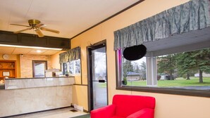 Un vestíbulo de hotel con una recepción, un sillón rojo, una mesa de mármol y vistas al exterior.