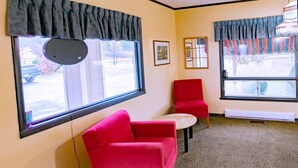Una habitación con un sofá rojo, una mesita redonda y dos ventanas con cortinas.