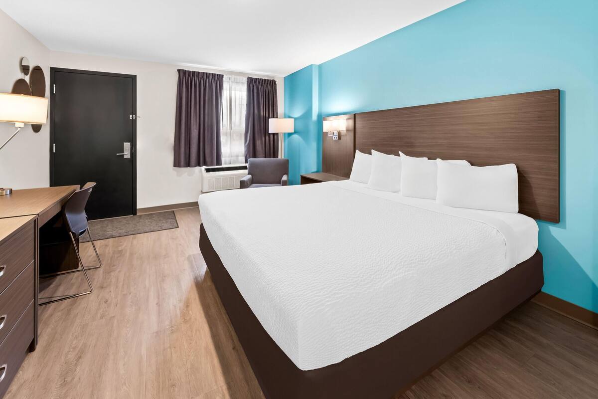 A hotel room with a large bed, a desk, a chair, and a window with curtains.