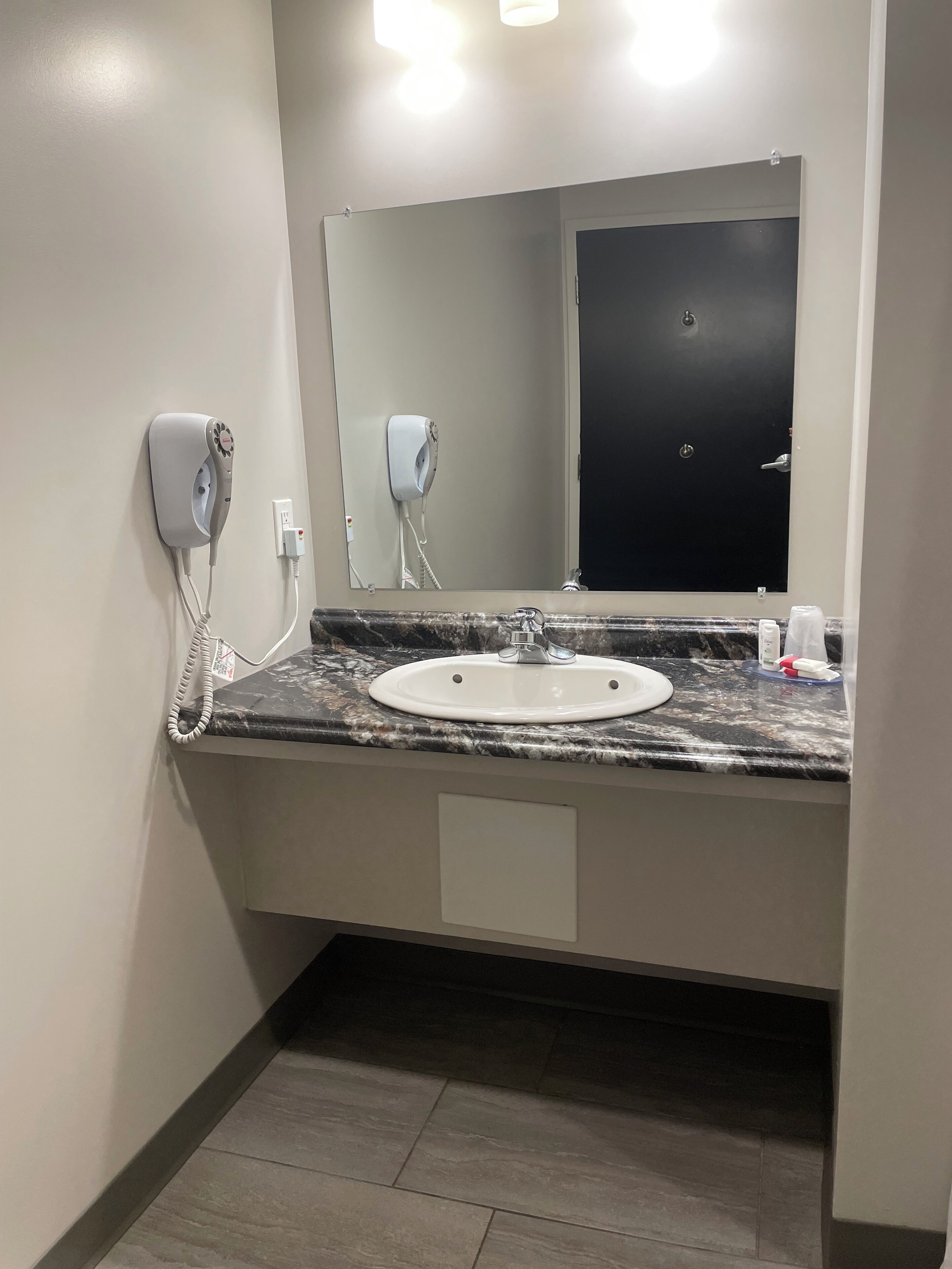 A bathroom with a marble countertop, a white sink, a mirror, and two hair dryers mounted on the wall.