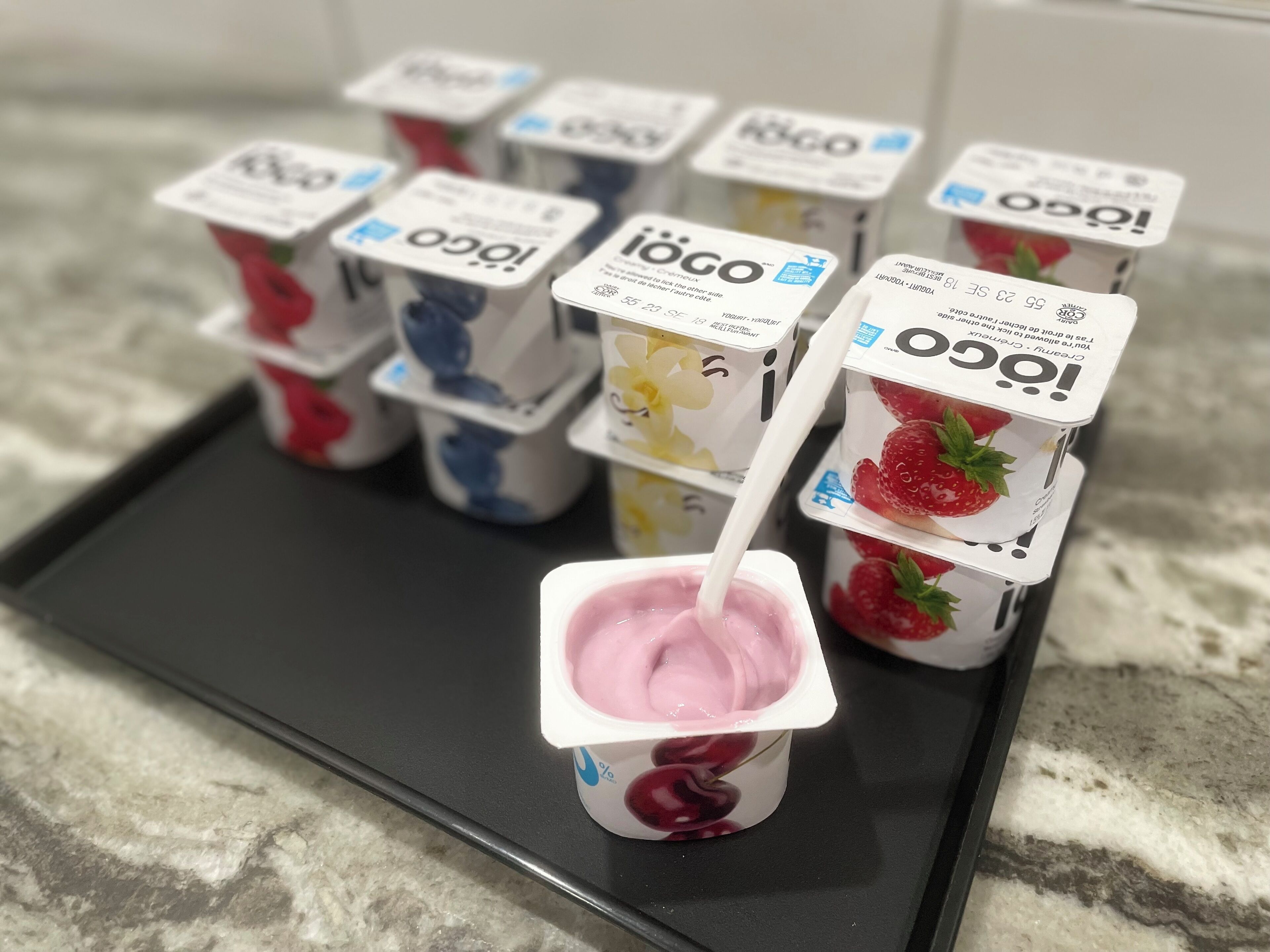 A tray with several containers of Ioca yogurt, some with fruit designs, and one with a pink yogurt.