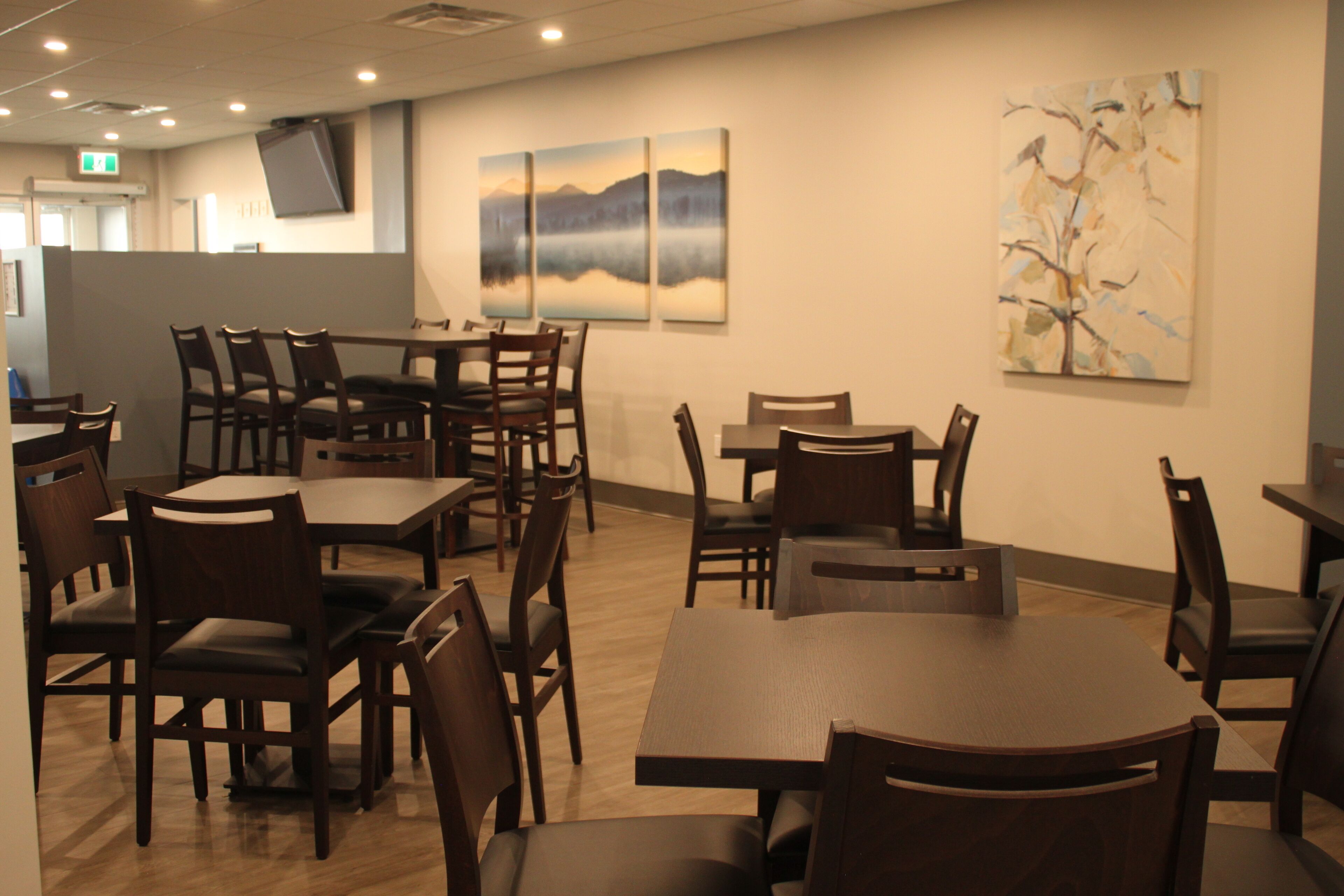A restaurant with wooden tables and chairs, a flat-screen TV on the wall, and paintings on the walls.