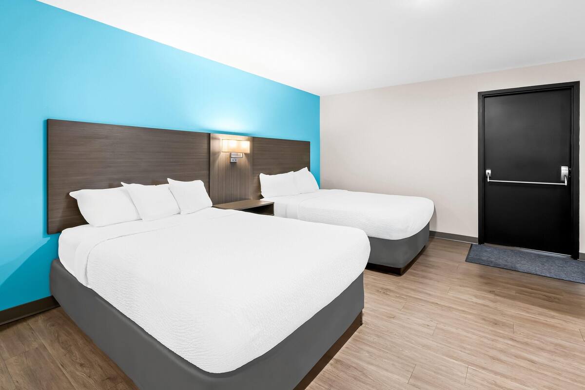 A hotel room with two beds, a wooden floor, and a blue accent wall.