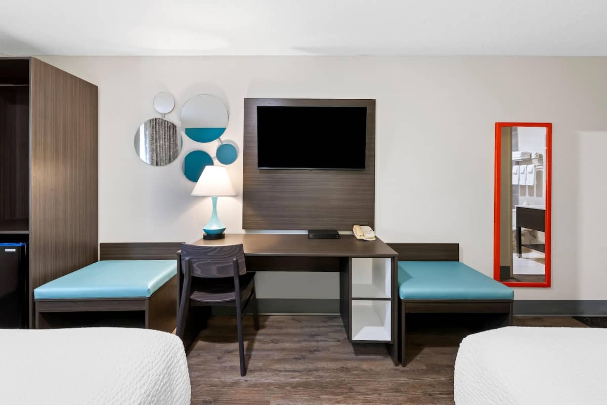 A hotel room with a bed, a desk with a chair, a TV, and a mirror.