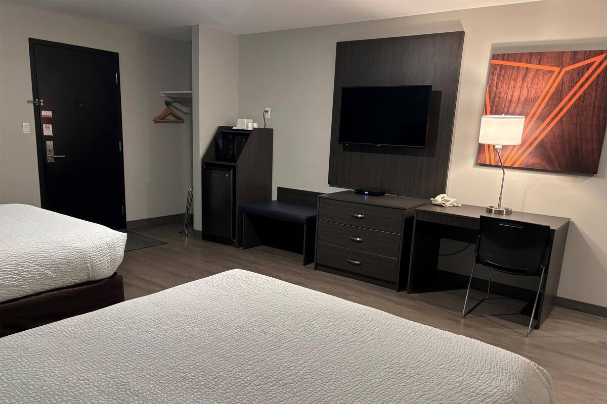 A hotel room with two beds, a desk with a chair, a TV, and a lamp.