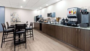A modern kitchen area with a long counter, microwave, coffee machine, and seating for four.