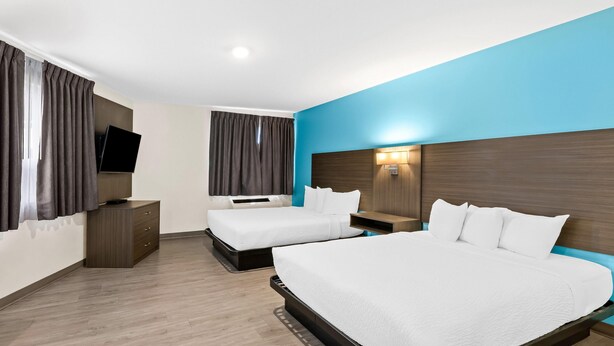 A hotel room with two beds, a TV, a nightstand, and a wooden dresser.