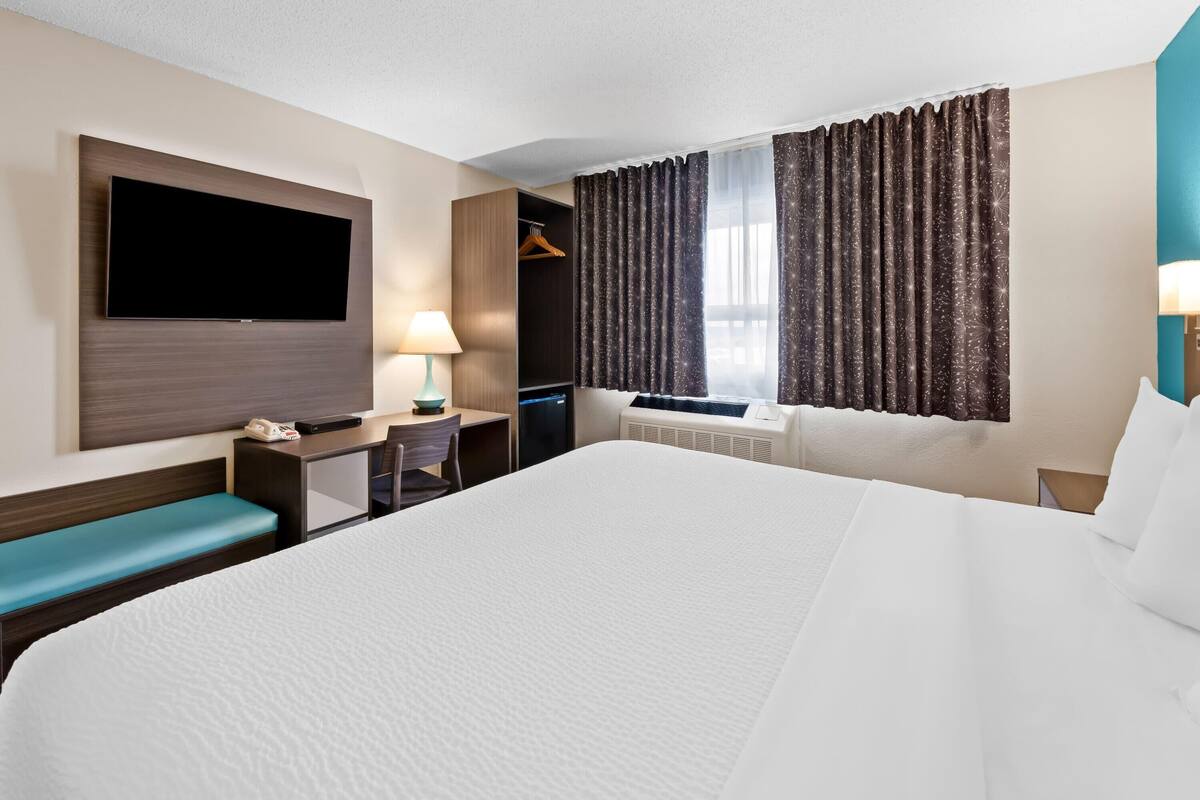 A hotel room with a large bed, a desk with a lamp, a TV mounted on the wall, and a wardrobe.