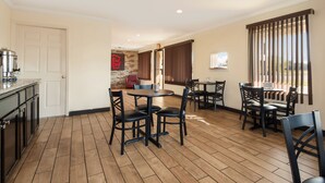 A dining area with wooden flooring, black chairs, and a round table. There is a kitchen area with a coffee machine and cabinets. - Red Roof Inn Santee (Santee)