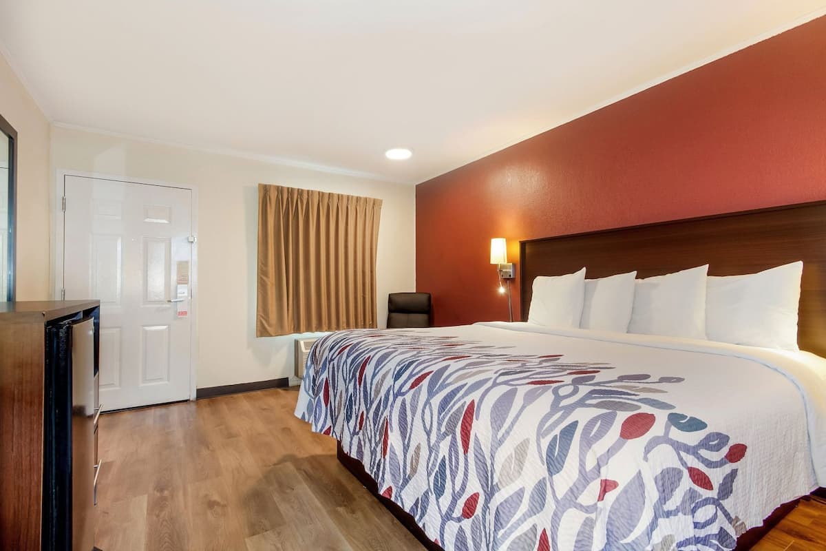 Ein Hotelzimmer mit Bett, Schreibtisch, Stuhl, Wandlampe und Tür.