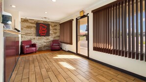 Una habitación con pared de piedra, un letrero que dice 'Red Roof Inn', dos sillones de cuero, piso de madera y una puerta corrediza de vidrio que da al exterior.
