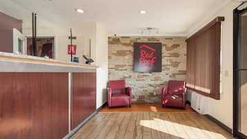Uma área de recepção com parede de pedra, duas poltronas de couro, um balcão com um dispositivo digital e uma placa da Red Roof Inn.
