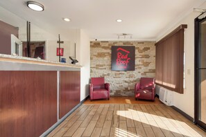 A reception area with a stone wall, two leather chairs, a counter with a digital device, and a sign for Red Roof Inn.
