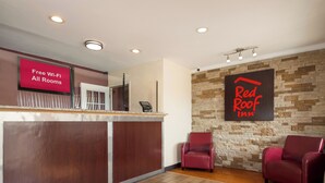 A hotel reception area with a wooden reception desk, a digital screen displaying 'Free Wi-Fi All Rooms,' and a 'Red Roof Inn' sign on the wall.