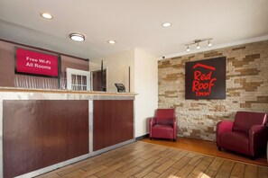 A hotel reception area with a wooden reception desk, a digital screen displaying 'Free Wi-Fi All Rooms,' and a 'Red Roof Inn' sign on the wall. - Red Roof Inn Santee (Santee)