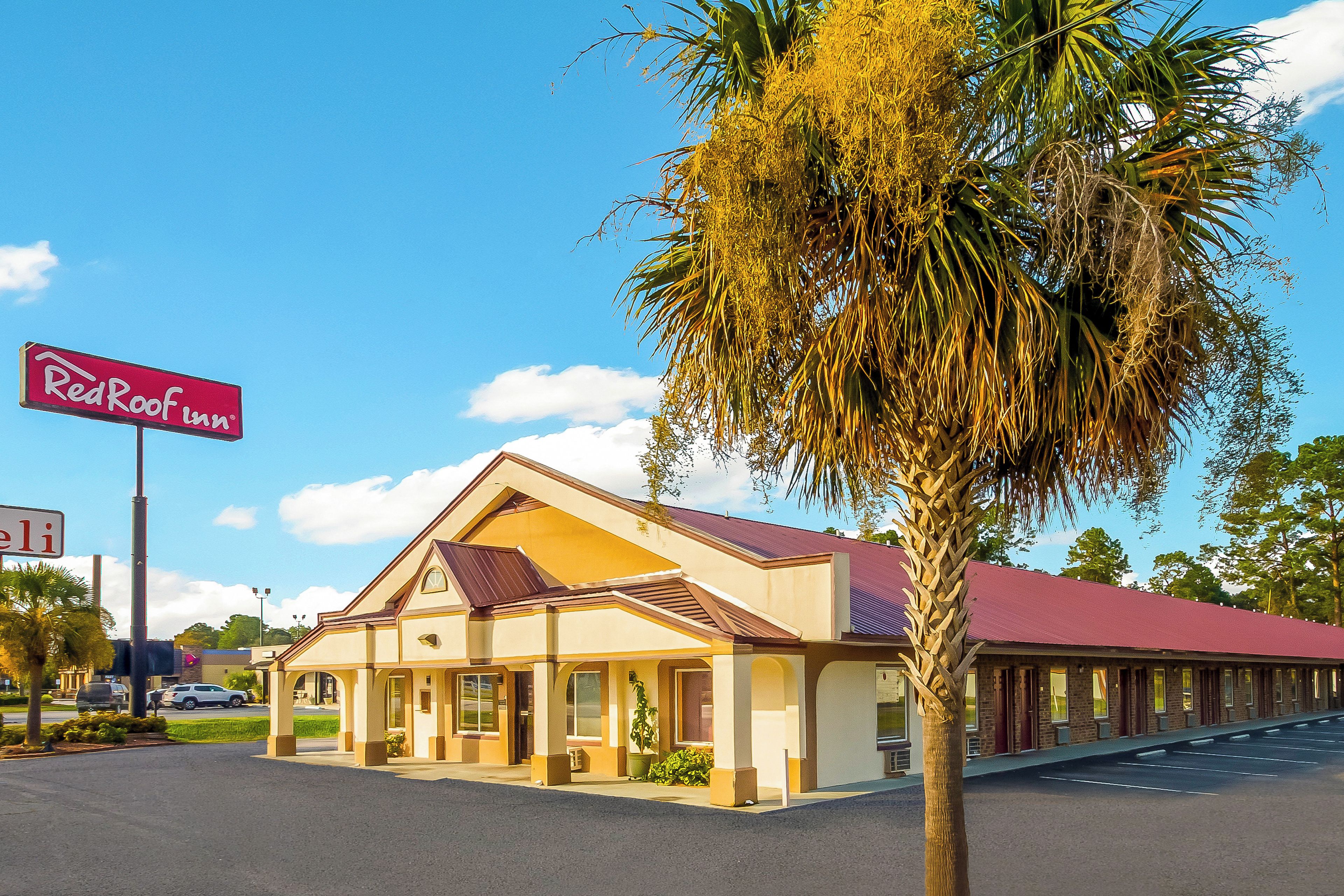 A Red Roof Inn with a single-story structure, a red roof, and a palm tree in front.