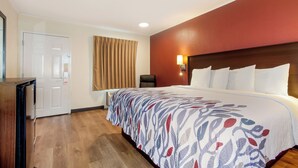 A hotel room with a bed, a desk, a chair, a door, and a window with curtains.