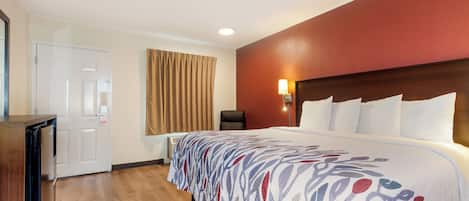 A hotel room with a bed, a desk, a chair, a door, and a window with curtains.