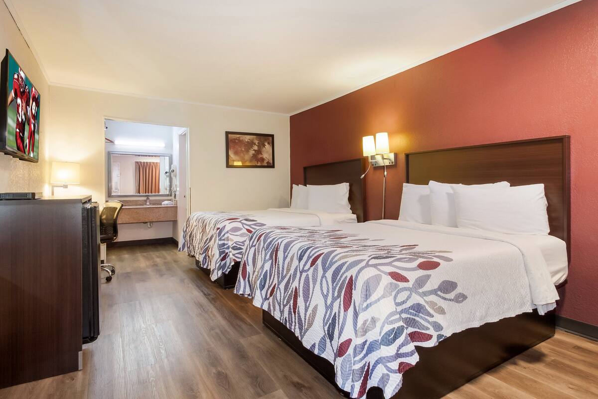 Ein Hotelzimmer mit zwei Betten, einem Schreibtisch, einem Spiegel und einem Bild an der Wand.