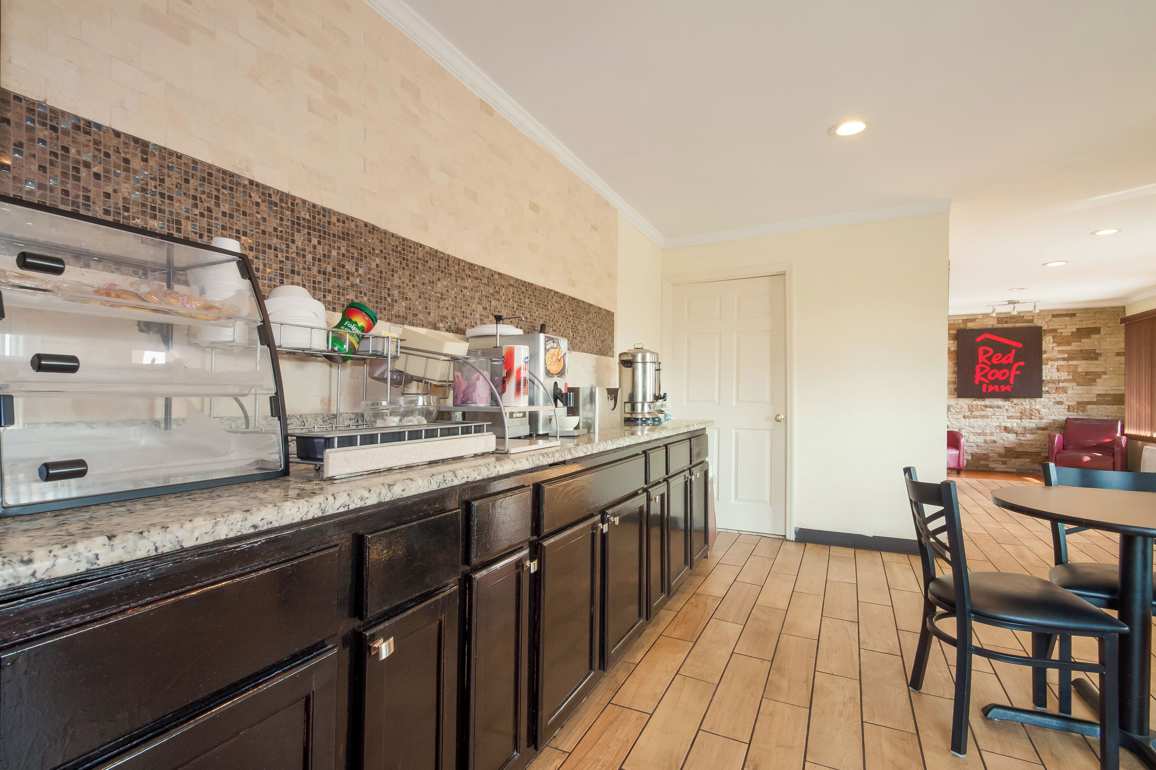 Una barra de desayuno con cafetera, tostadora y refrigerador. Hay una puerta que conduce a un comedor con mesa y sillas.