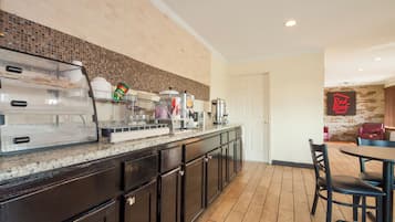 Una barra de desayuno con cafetera, tostadora y refrigerador. Hay una puerta que conduce a un comedor con mesa y sillas.