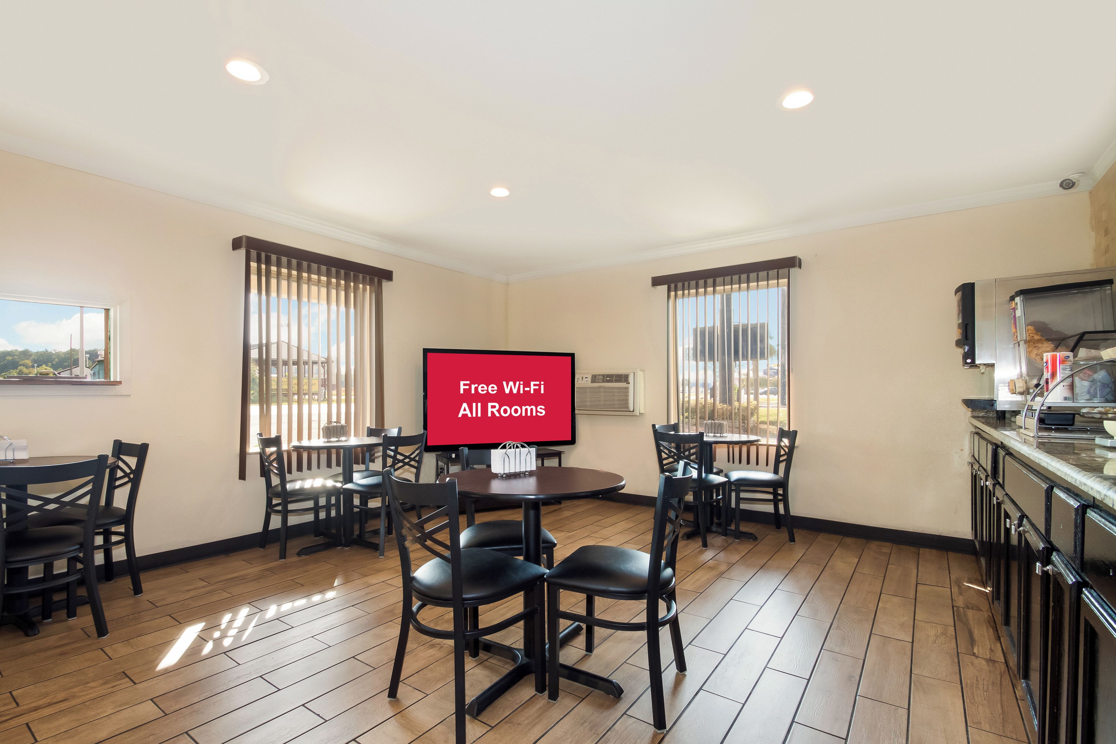 A hotel room with a dining area, a TV screen displaying 'Free Wi-Fi All Rooms,' and a kitchen area.