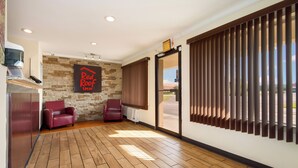 A spacious room with a wooden floor, two red leather chairs, a stone wall with a 'Red Roof TAXI' sign, and a large window with blinds. - Red Roof Inn Santee (Santee)