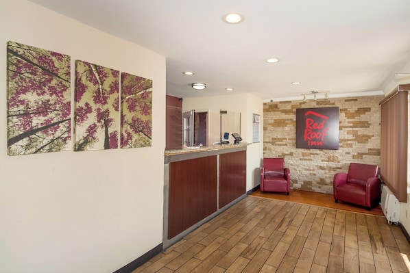 A reception area with a wooden floor, a reception desk, and two red leather chairs.