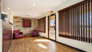 Una habitación con pared de piedra, un letrero que dice 'Red Roof Inn', dos sillones de cuero, piso de madera y un patio de vidrio corredizo.