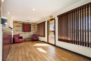 Una habitación con pared de piedra, un letrero que dice 'Red Roof Inn', dos sillones de cuero, piso de madera y un patio de vidrio corredizo.